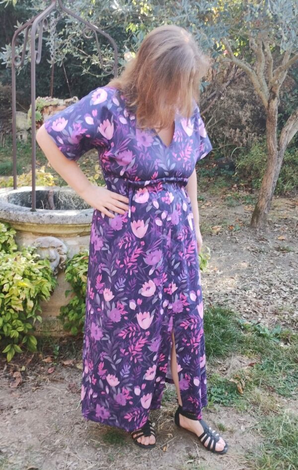 Vue de 3/4 face d'une femme portant la robe longue manches courtes motif fleurs violettes