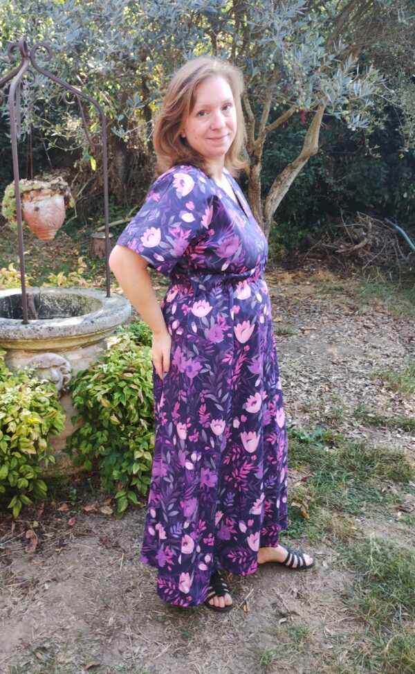Vue de 3/4 profil droit d'une femme portant la robe longue manches courtes motif fleurs violettes